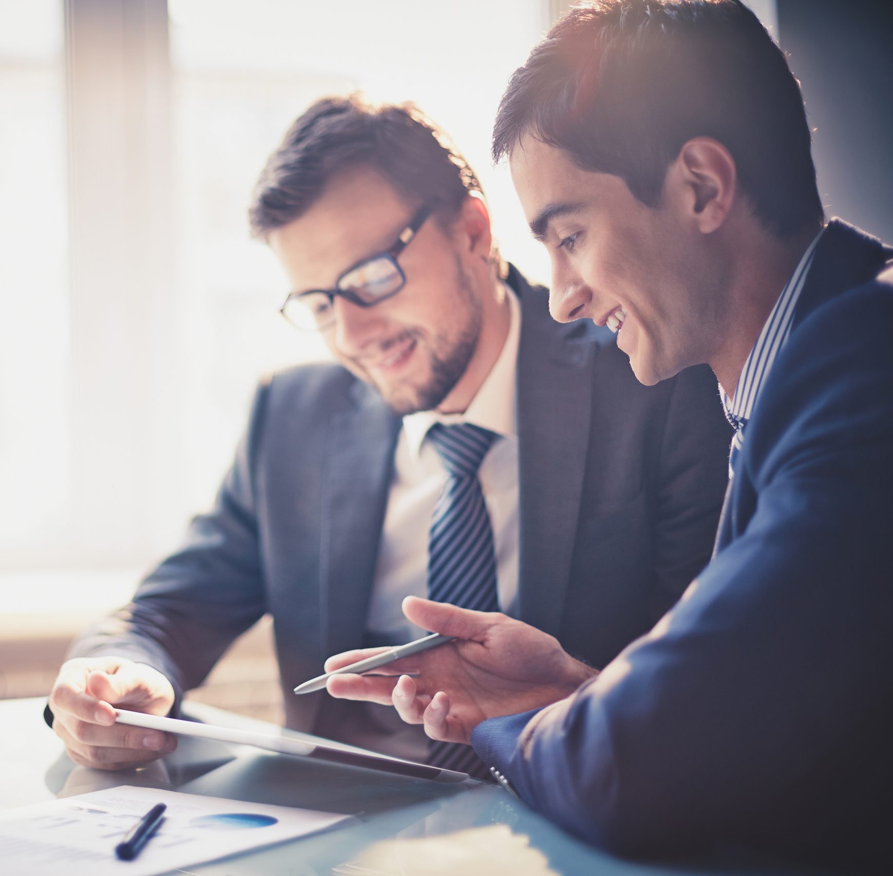 Image of two young businessmen using touchpad at meeting